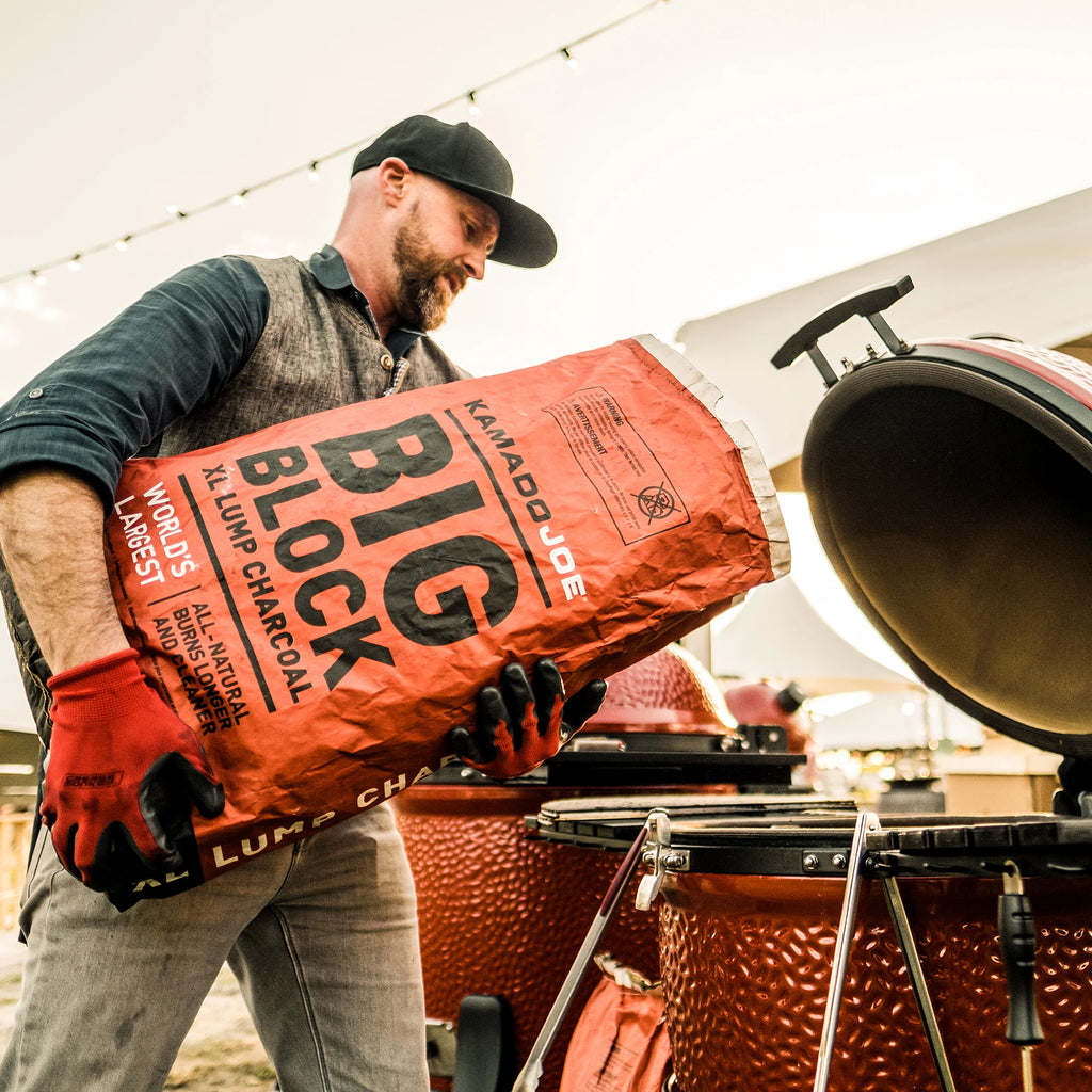 A man pours big block charcoal from the bag into a Kamado Joe grill