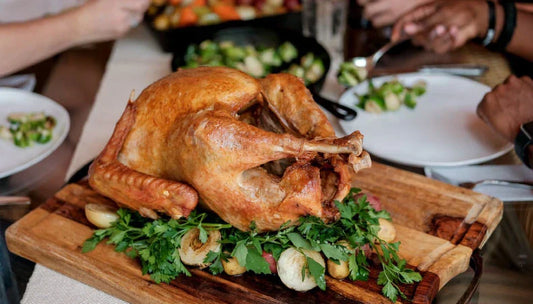 Roasted turkey on a wooden cutting board with people around a table setting.