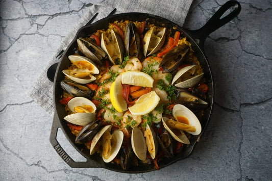 A seafood bake featuring mussels and topped with fresh chopped herbs and lemon wedges