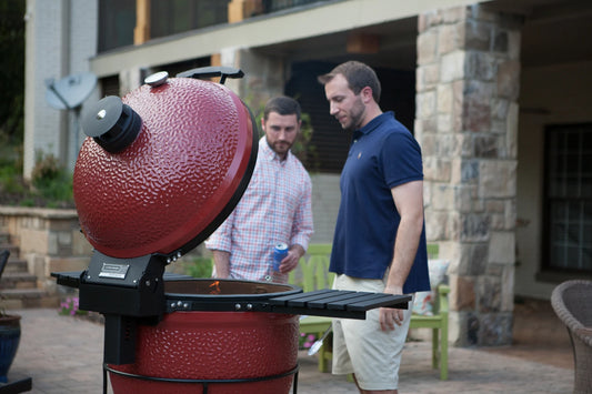 2 young white men look at an open Kamado Joe grill that has a small flame coming out of the grill body