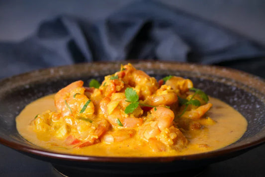 A bowl of shrimp in a yellow curry sauce and topped with chopped fresh herbs