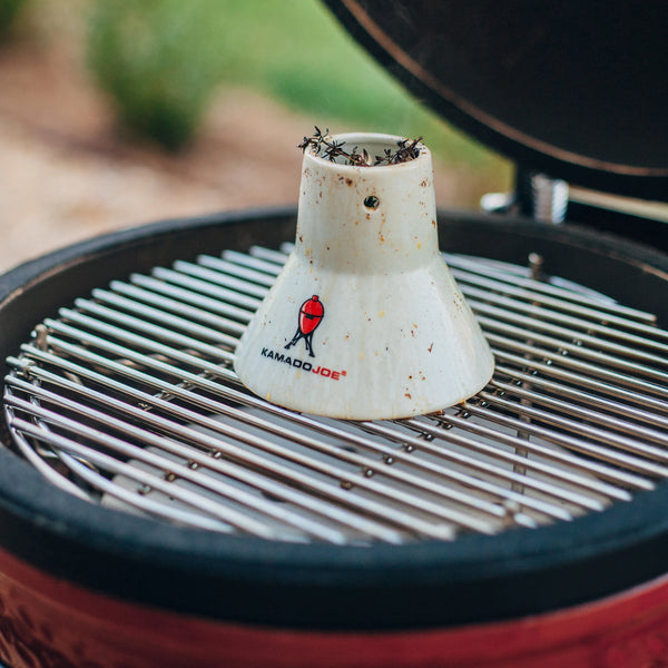 Kamado Joe chicken stand on the cooking grate in a Kamado Joe grill. The stand is full of aromatic herbs and covered with juices after a cook.