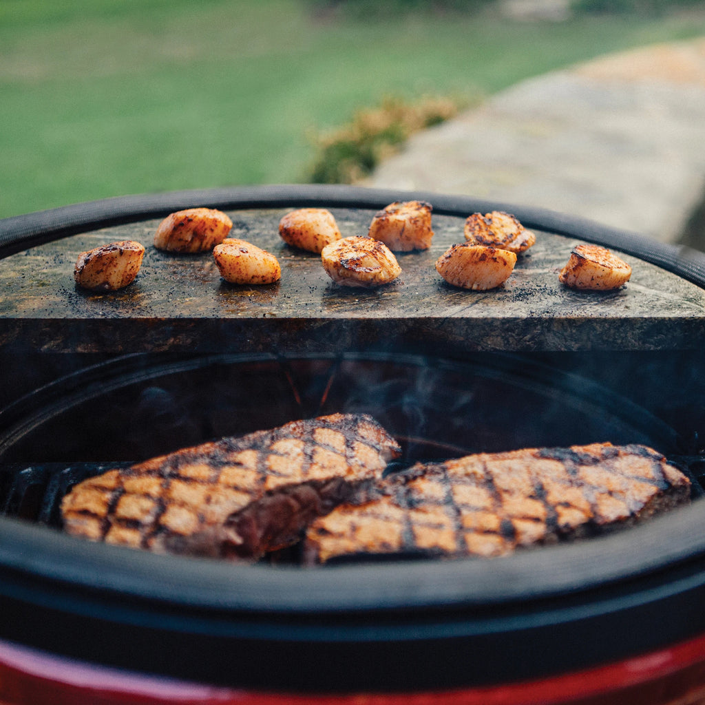Scallops cook on a half-moon soapstone installed on the top rack of a Divide & Conquer system while steaks sear on a half-moon cast iron grate on the lower tier.