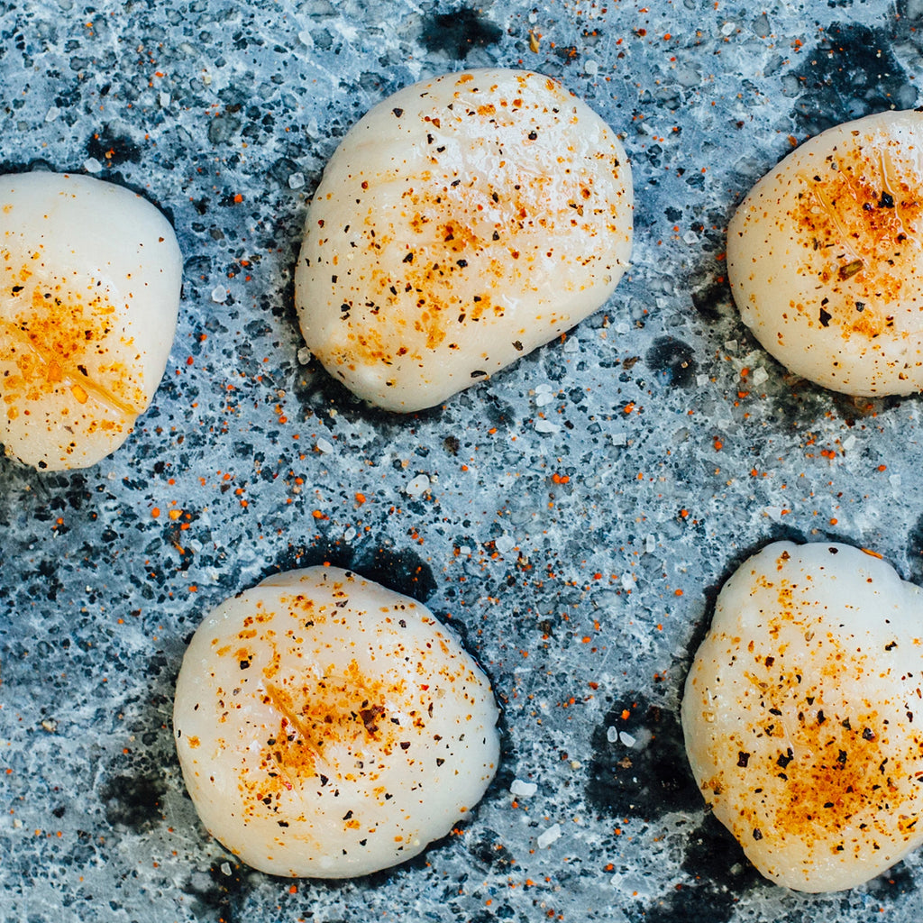 Closeup of seasoned scallops cooking on a soapstone