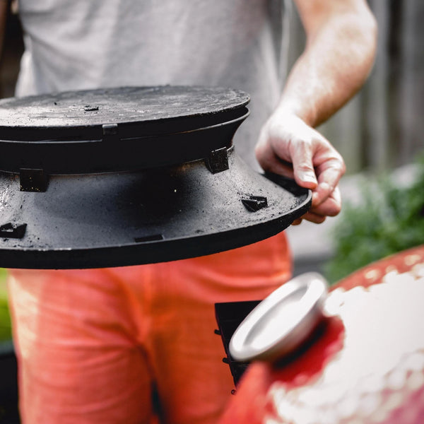 A man carries the base of a SloRoller towards a Kamado Joe grill.