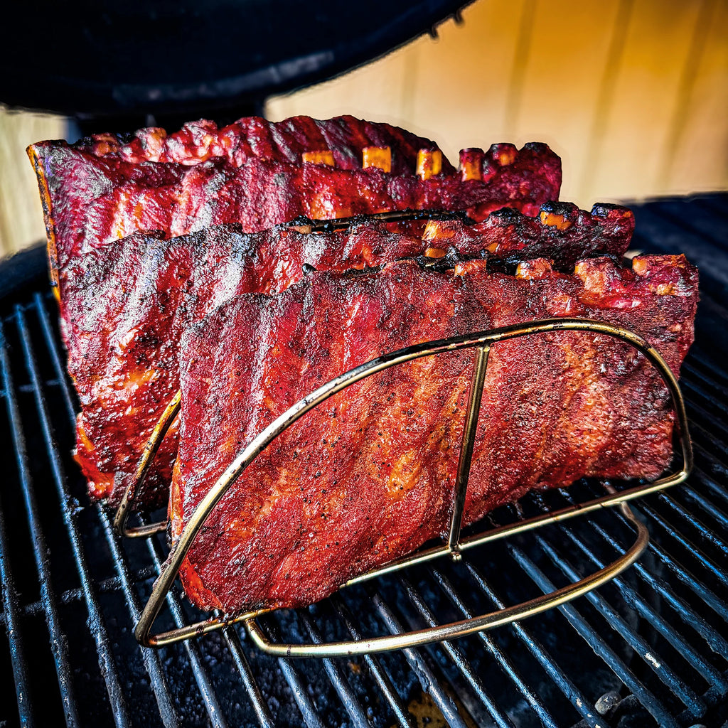 4 cooked racks of ribs stand in a Kamado Joe rib rack on the cooking grate of a Kamado Joe grill