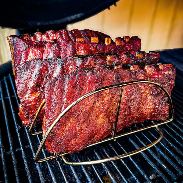 4 cooked racks of ribs stand in a Kamado Joe rib rack on the cooking grate of a Kamado Joe grill