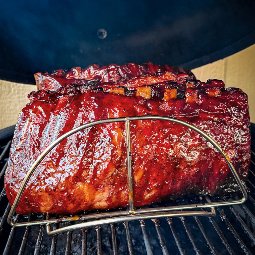 2 cooked and sauced racks of ribs stand in a Kamado Joe rib rack on the grate of a Kamado Joe grill