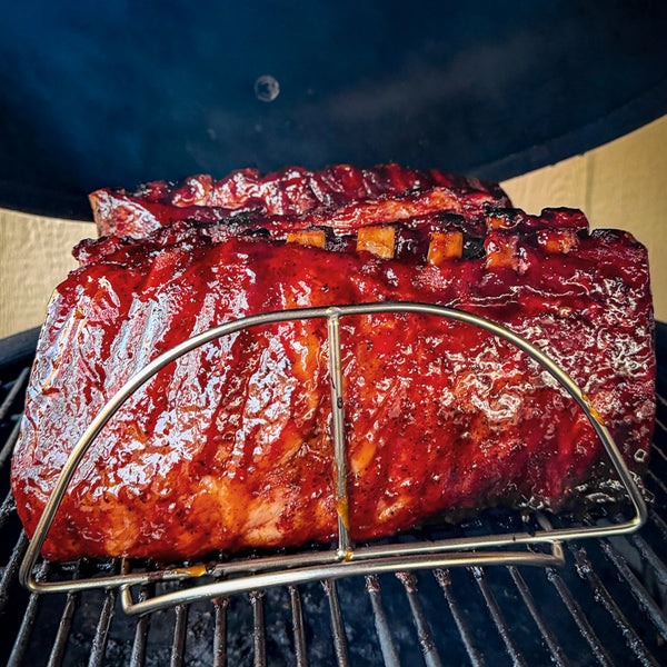 2 cooked and sauced racks of ribs stand in a Kamado Joe rib rack on the grate of a Kamado Joe grill