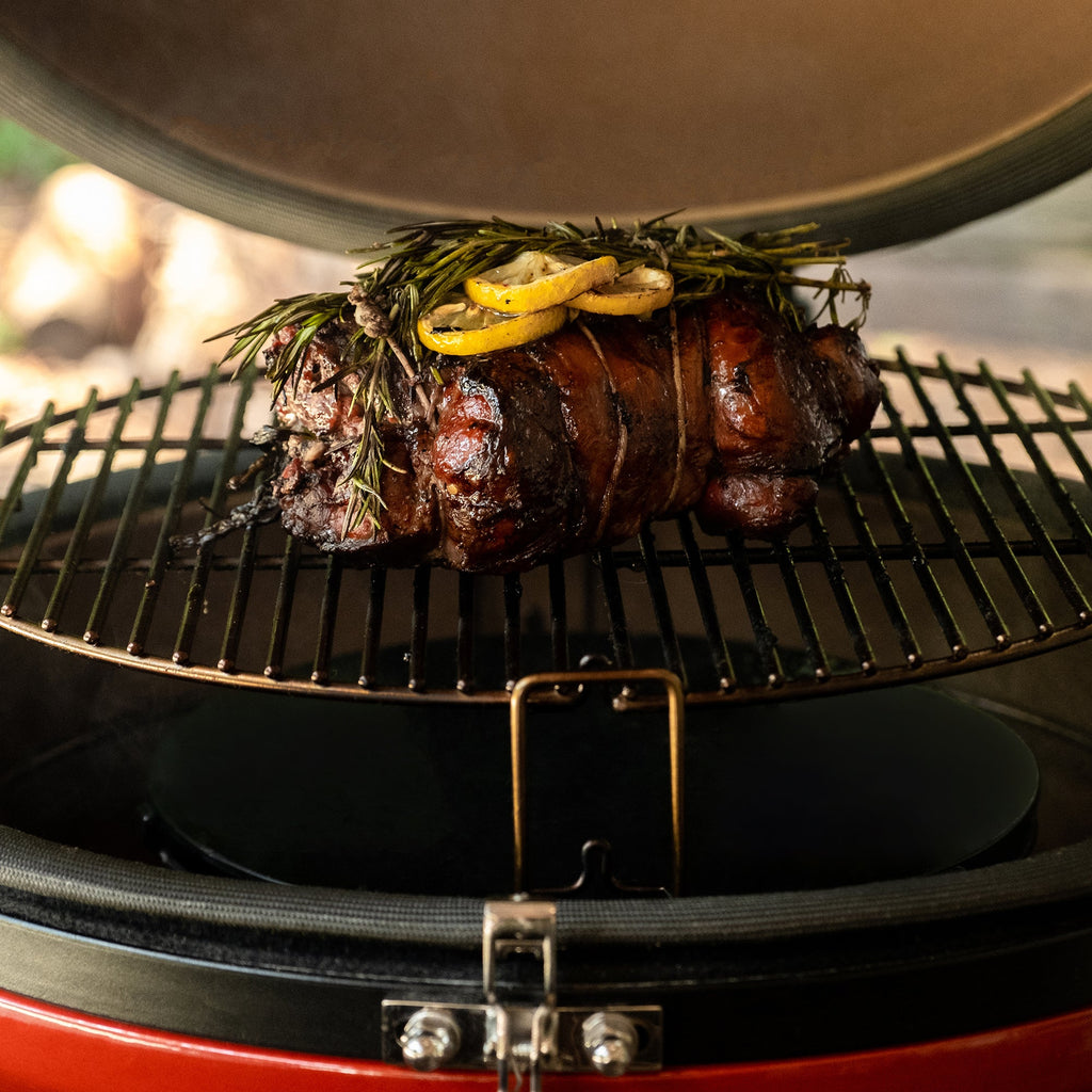 A smoked pork roast topped with fresh herbs and lemon slices sits on the grill of an open Big Joe III grill.