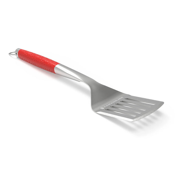 A Kamado Joe stainless steel spatula with dimpled red handle lying on a white surface