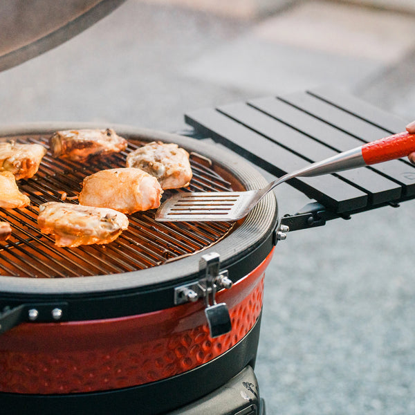 Someone using the Kamado Joe spatula to turn chicken thighs cooking in a Kamado Joe grill