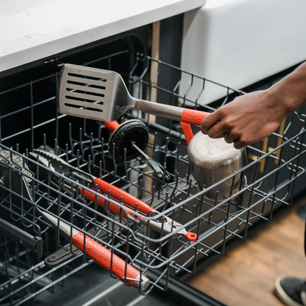 Loading the tools into a the top rack of a dishwasher. The tongs, spatula, brush, basting pot and basting brush all fit together in the top rack.