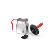 Steel basting pot with red handle sitting next to the combined brush/pot lid all against a white background.