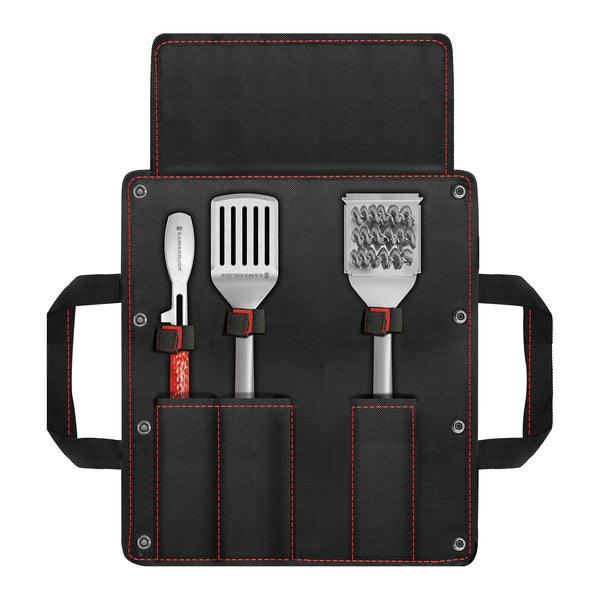 Set of three Kamado Joe kitchen tools (tongs, spatula, bristle brush) in a black carrying case with red stitching and side handled on a white background