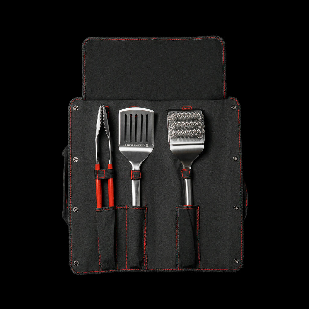 The inside of the canvas case showing the pockets for three tools. From left to right: tongs, spatula, and bristle brush. The case has red accent stitching around the edges, the pockets, and the loop that keep the tools in place. There is a flap attached to the top of the case that folds down over the heads of the tools to protect them when the case is folded for carrying.