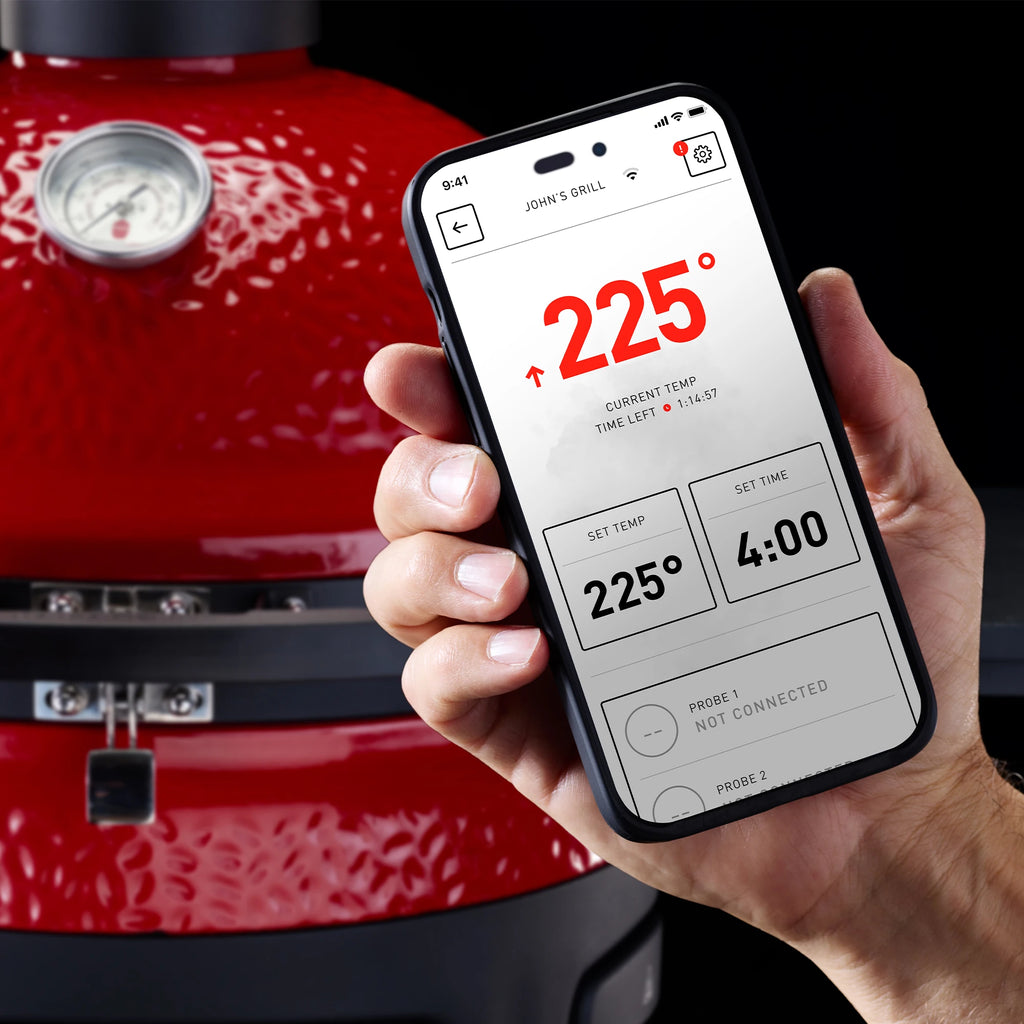 A hand holds a smartphone with the Kamado Joe app open on it. Use the app to control the Pellet Joe, which is shown in the background.