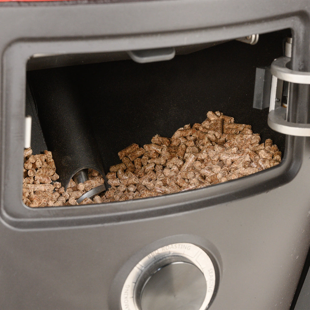 The door to the pellet hopper is just above the temperature dial. The door is open to show the hopper full of pellets and the auger that feeds pellets to the grill.