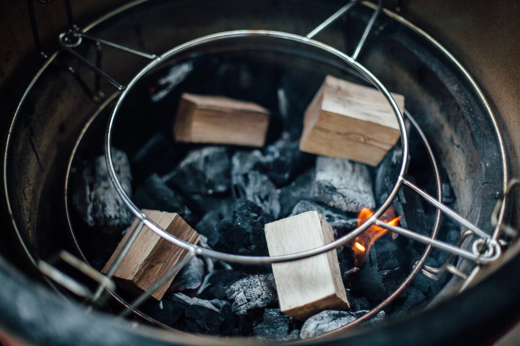 4 large chunks of wood arranged on tope of a pile of coals inside a Kamado Joe grill. There is a small flame coming up from one lump of charcoal.