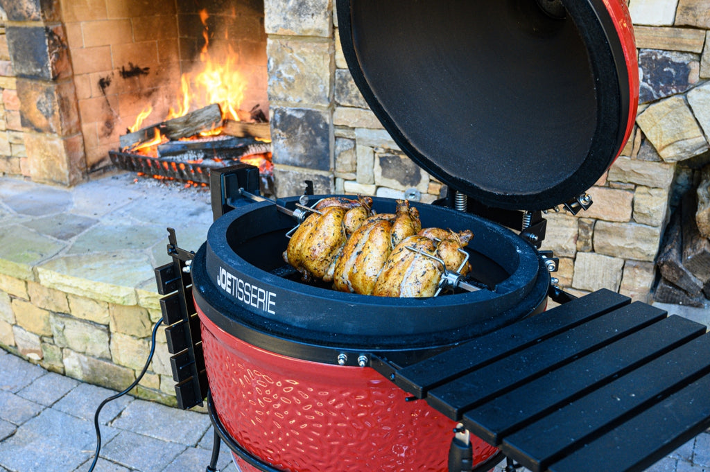 Three chickens roasting on the Kamado Joe rotisserie, called the JoeTisserie, next to an outdoor fireplace