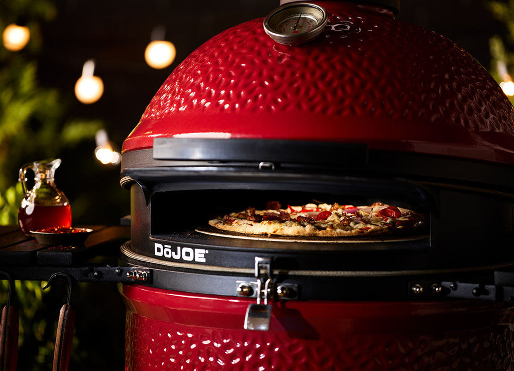 A pizza can be seen baking inside a DoJoe installed in a Kamado Joe grill.